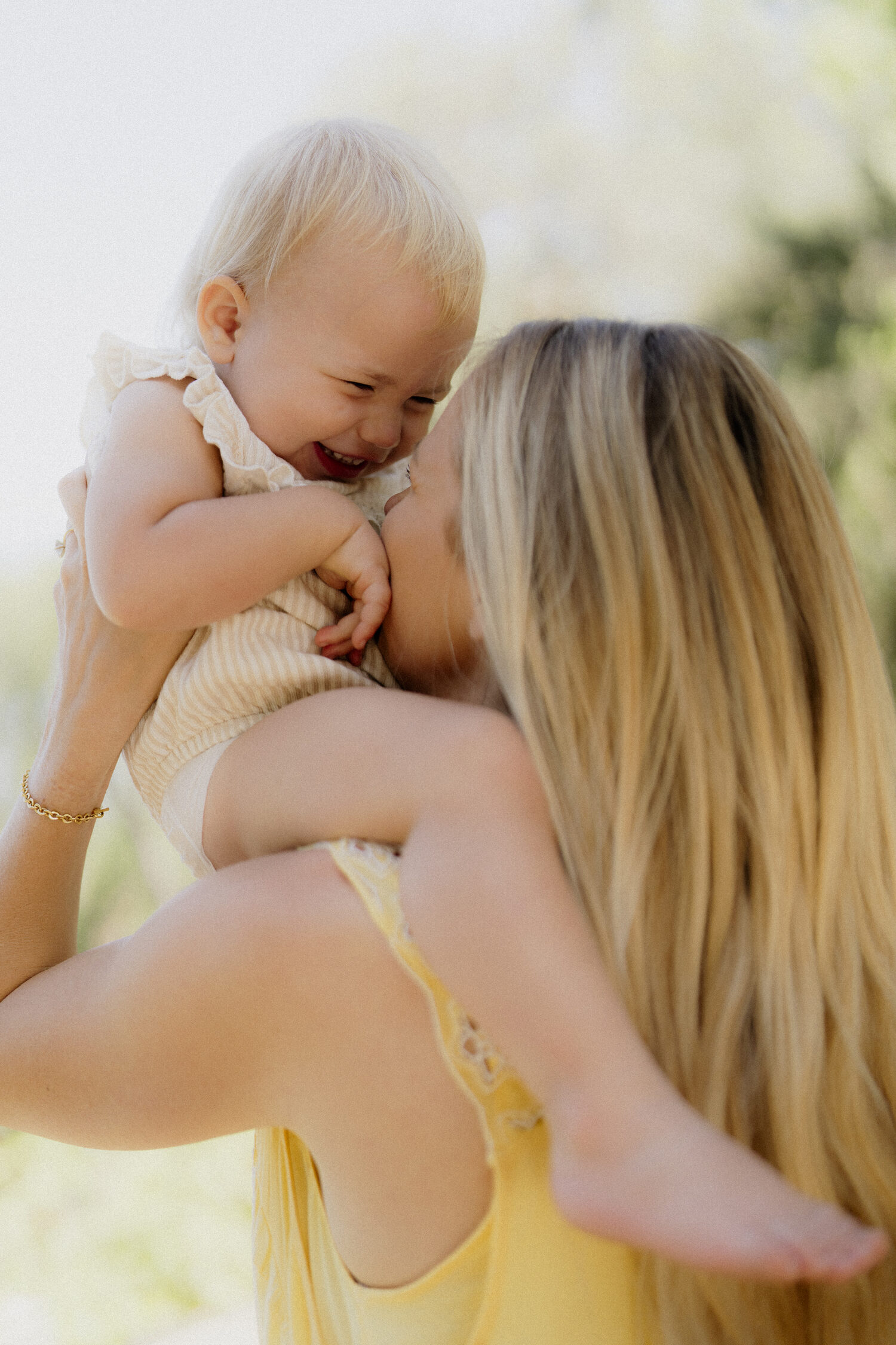 A mother in a yellow dress lifting her laughing baby in the golden afternoon light
