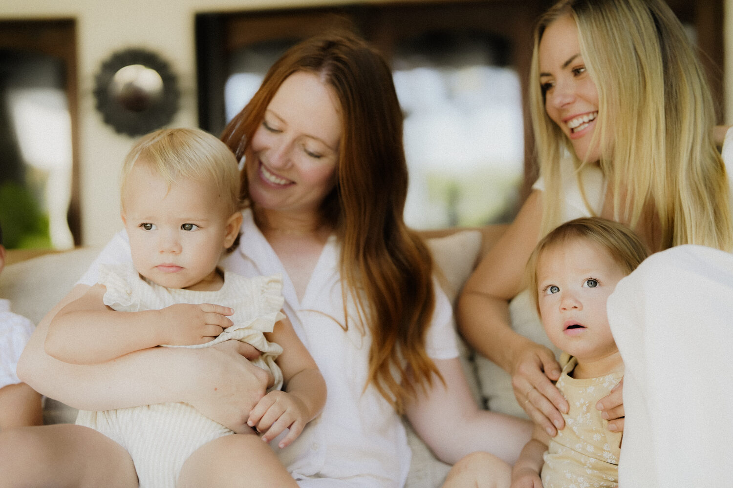 Two mothers sitting together, each holding her baby, laughing in warm light